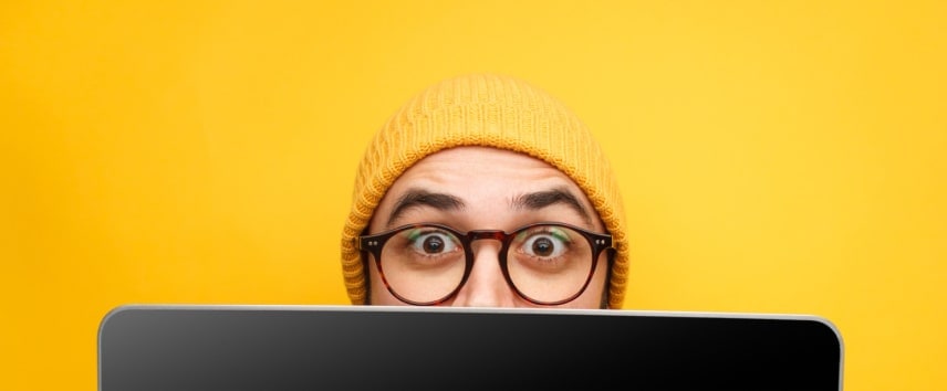 Person in a yellow hat peering over a laptop screen